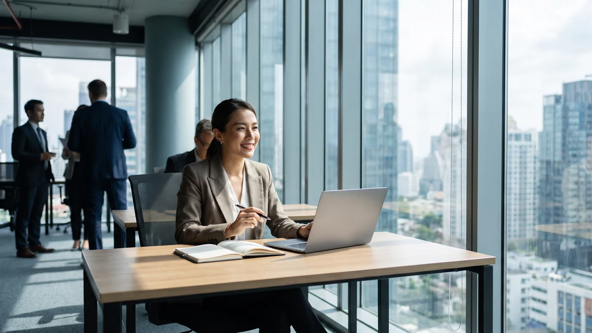 Professional executive assistant working on laptop in modern high-rise office with city view
