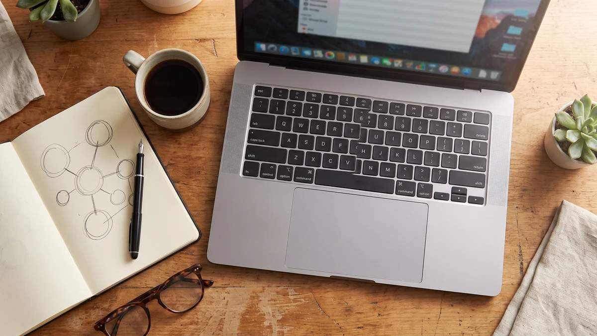 Overhead flat-lay of a laptop keyboard beside a notepad with a hand-drawn network diagram on a wooden desk